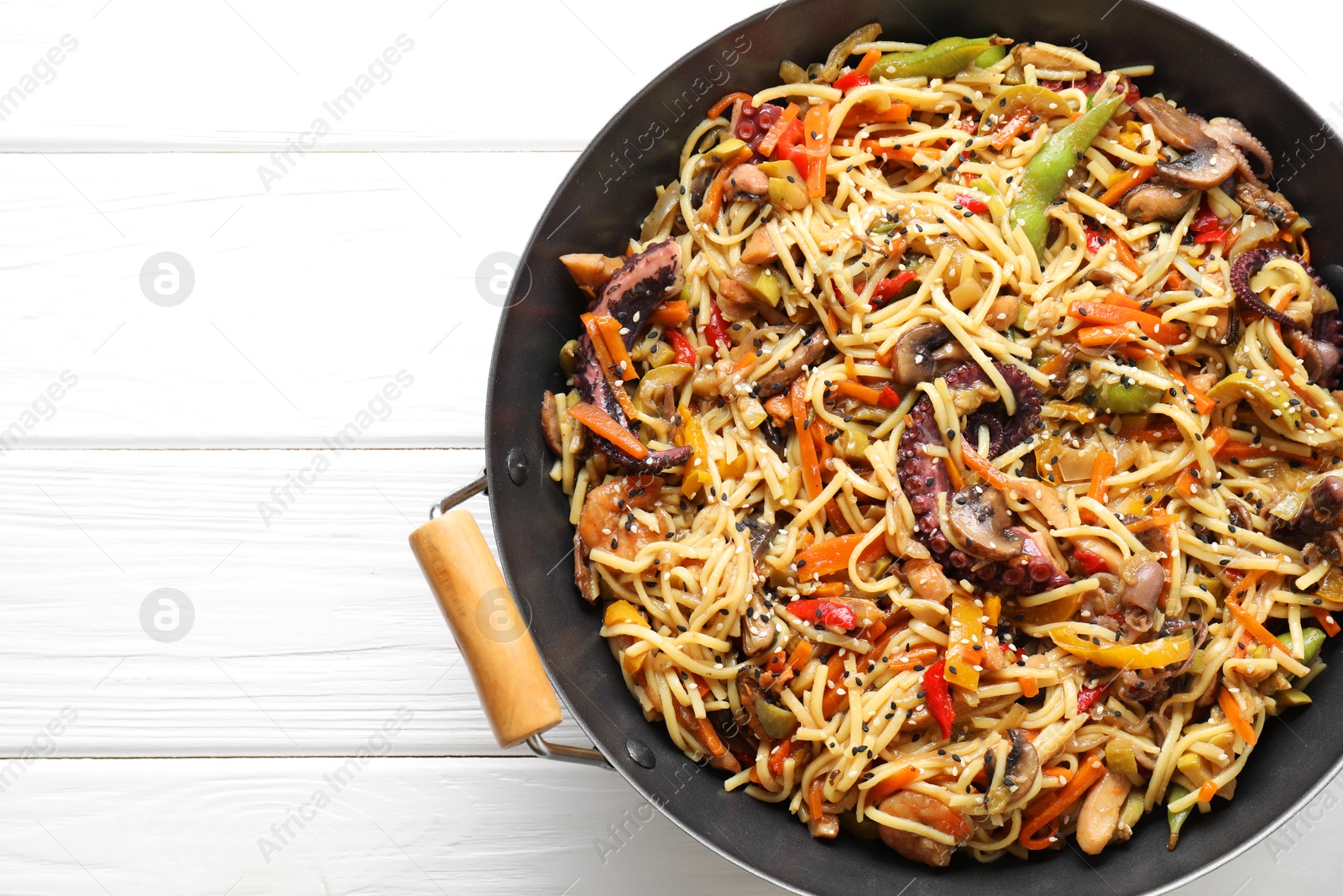 Photo of Stir-fry noodles with sea food and vegetables in wok on white wooden table, top view. Space for text