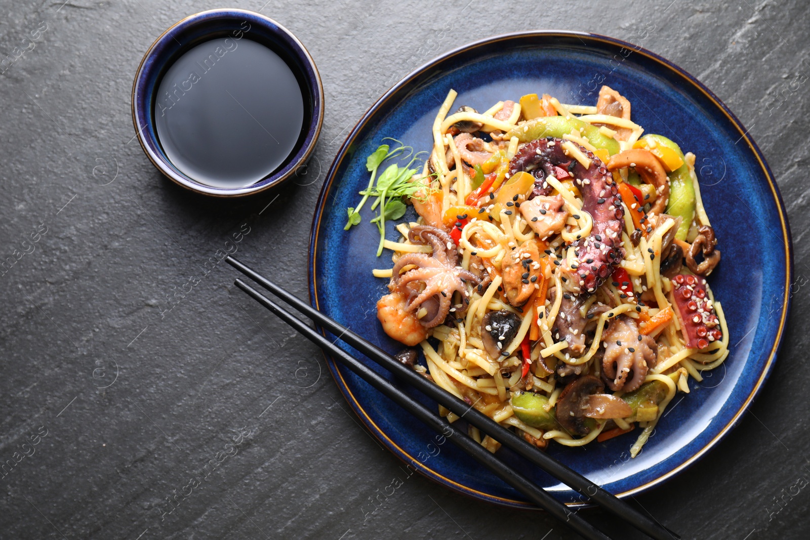 Photo of Stir-fry noodles with sea food, vegetables and soy sauce on dark textured table, top view