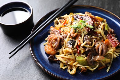 Photo of Stir-fry noodles with sea food, vegetables and soy sauce on dark textured table, closeup