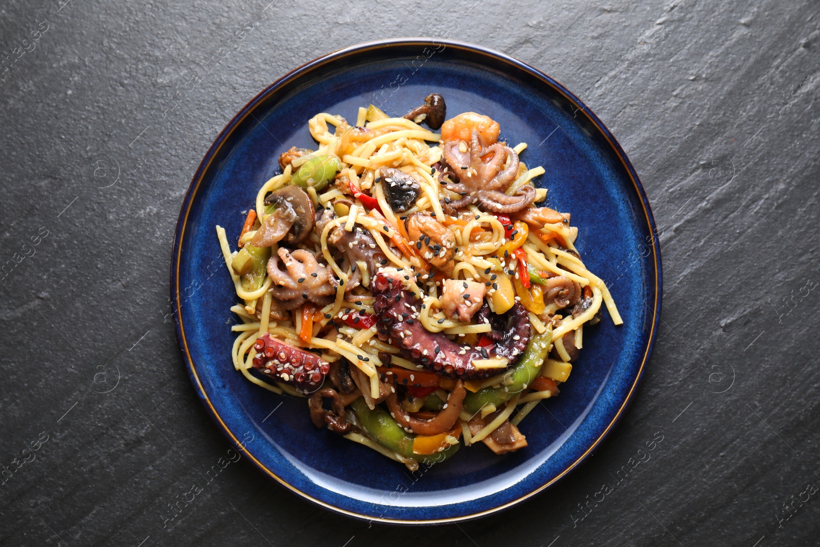 Photo of Stir-fry noodles with sea food and vegetables on dark textured table, top view