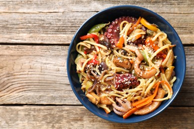 Photo of Stir-fry noodles with sea food and vegetables on wooden table, top view. Space for text