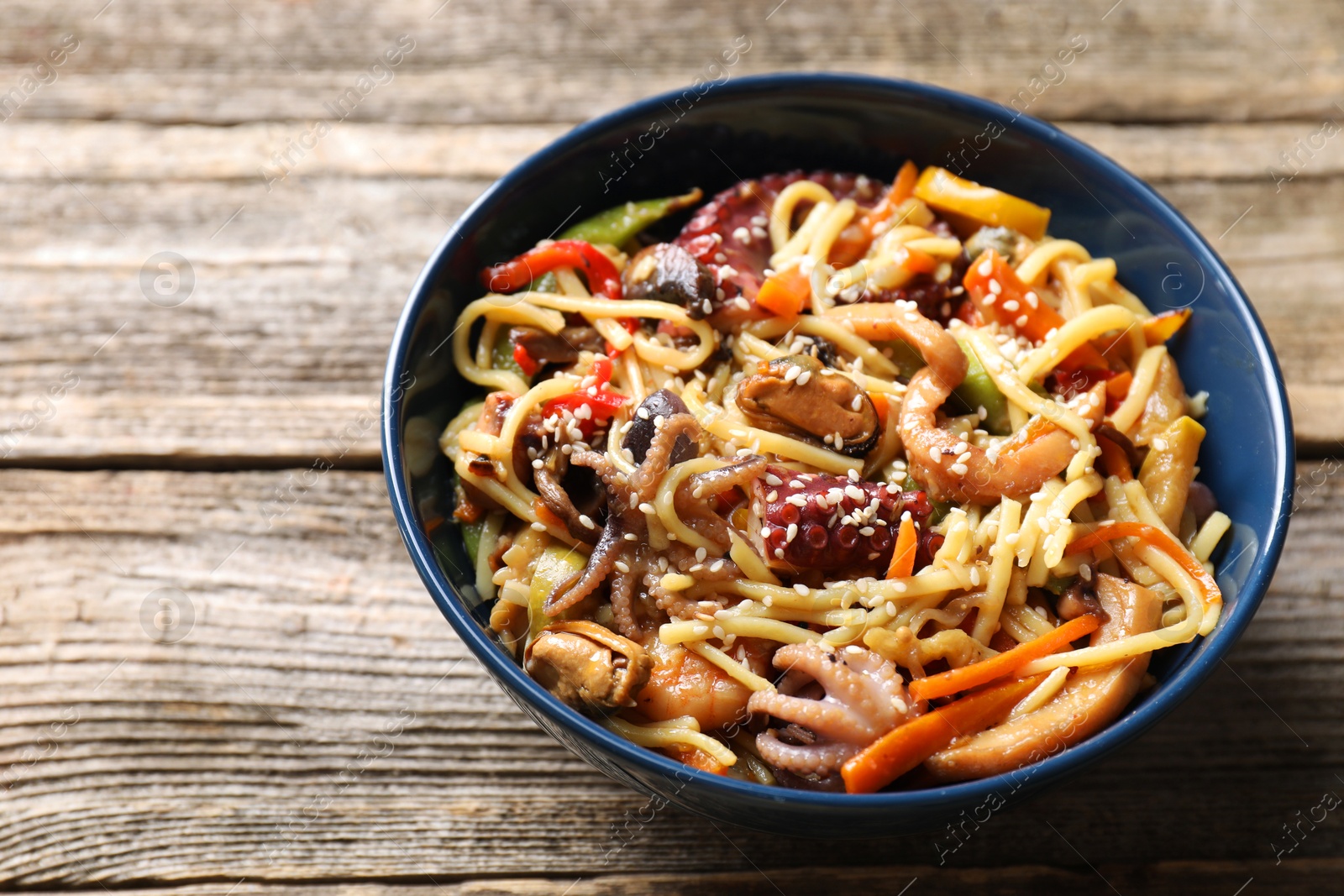 Photo of Stir-fry noodles with sea food and vegetables on wooden table, closeup. Space for text