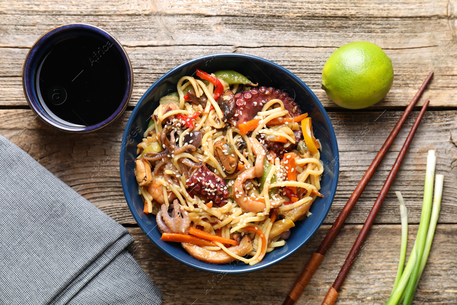 Photo of Stir-fry noodles with sea food and vegetables served on wooden table, flat lay