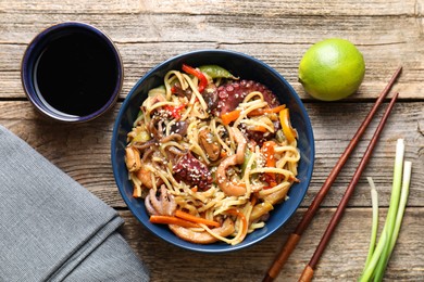 Photo of Stir-fry noodles with sea food and vegetables served on wooden table, flat lay