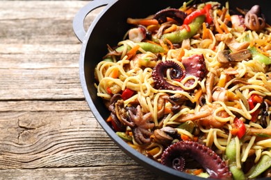 Photo of Stir-fry noodles with sea food and vegetables in wok on wooden table, closeup