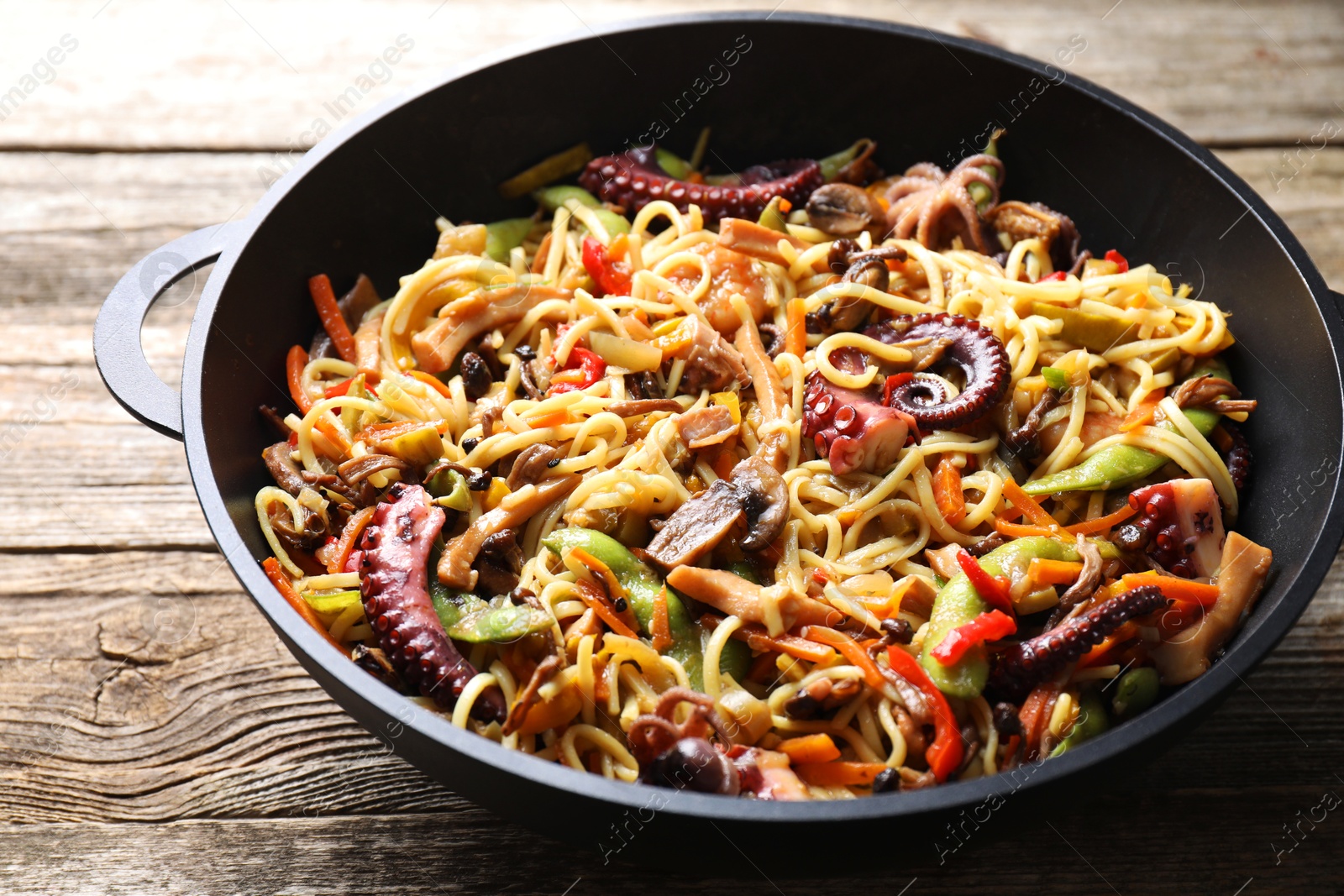 Photo of Stir-fry noodles with sea food and vegetables in wok on wooden table, closeup