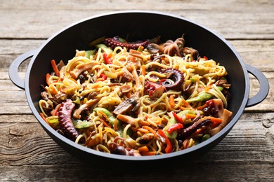 Photo of Stir-fry noodles with sea food and vegetables in wok on wooden table, closeup