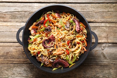 Photo of Stir-fry noodles with sea food and vegetables in wok on wooden table, top view