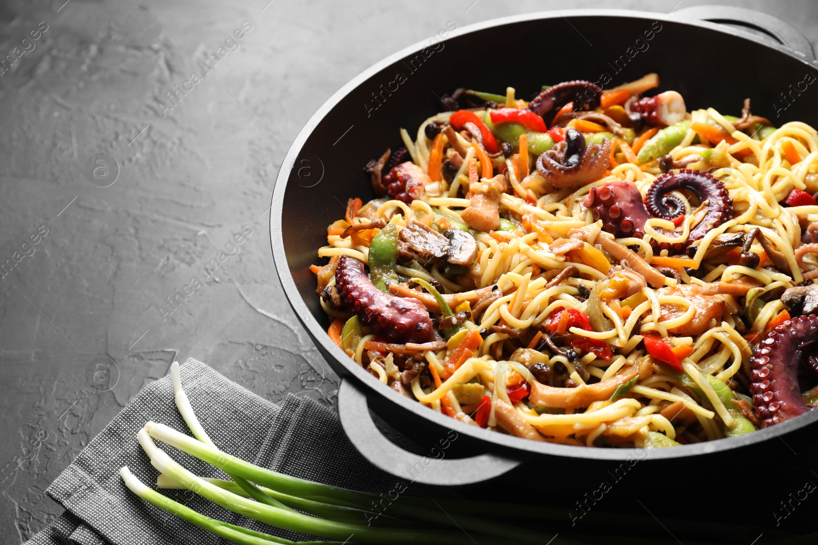 Photo of Stir-fry noodles with sea food and vegetables in wok on dark textured table, closeup