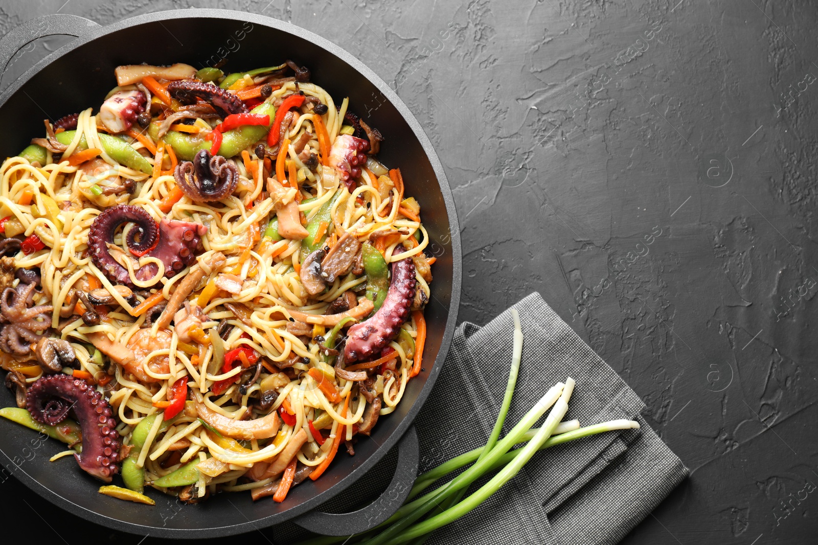 Photo of Stir-fry noodles with sea food and vegetables in wok on dark textured table, top view. Space for text