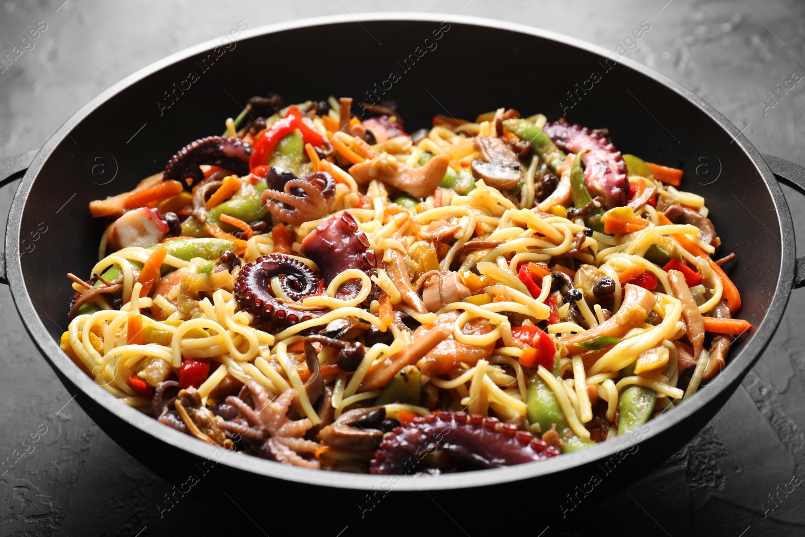 Photo of Stir-fry noodles with sea food and vegetables in wok on dark textured table, closeup