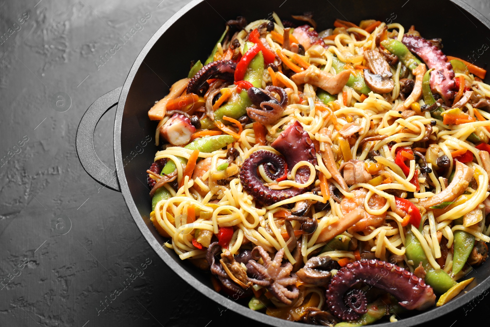 Photo of Stir-fry noodles with sea food and vegetables in wok on dark textured table, closeup