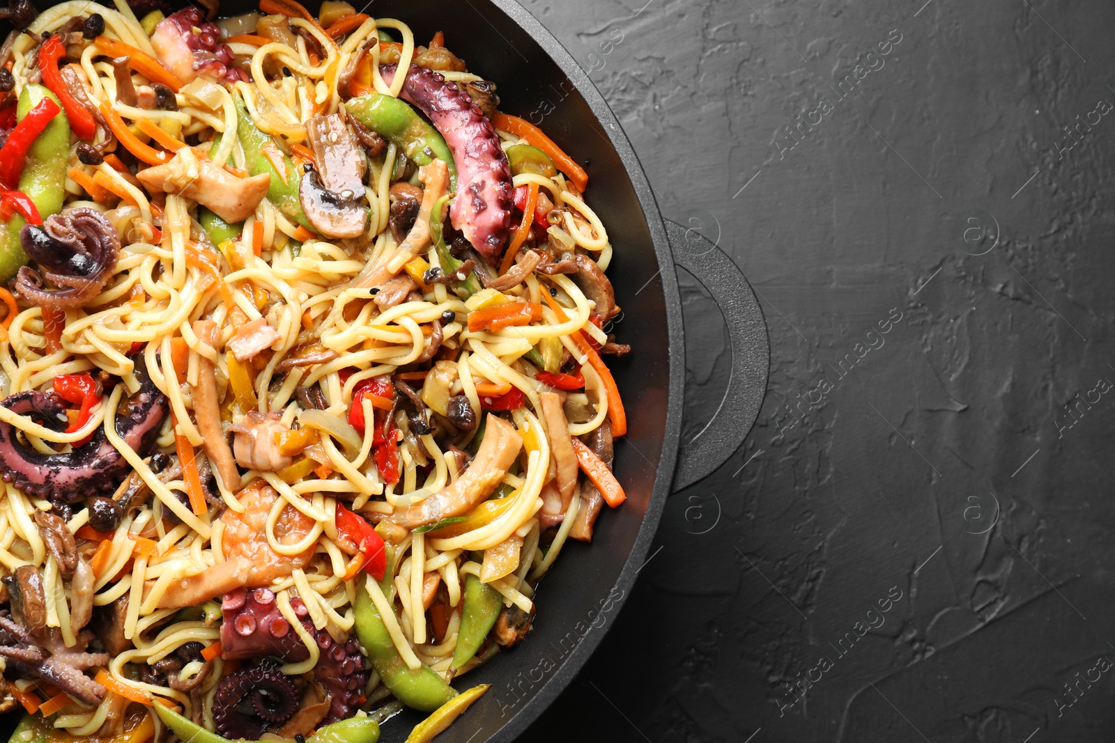 Photo of Stir-fry noodles with sea food and vegetables in wok on dark textured table, top view. Space for text