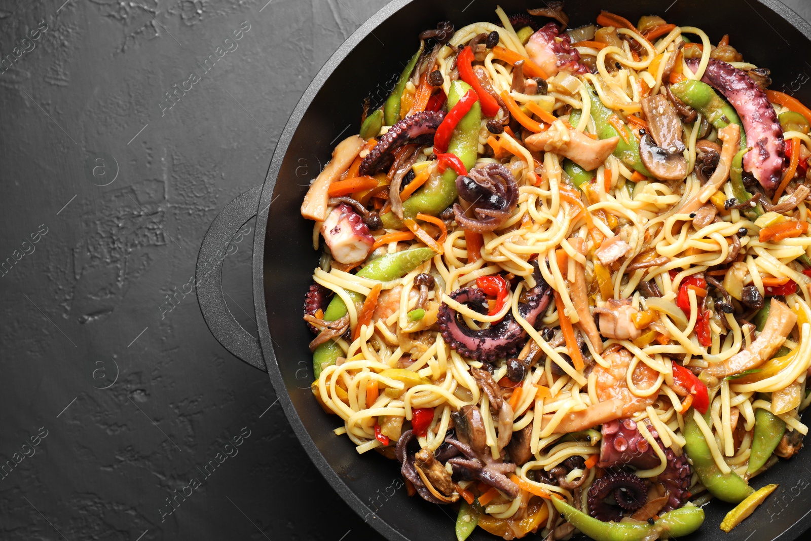 Photo of Stir-fry noodles with sea food and vegetables in wok on dark textured table, top view. Space for text