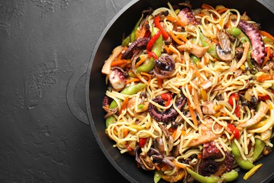 Photo of Stir-fry noodles with sea food and vegetables in wok on dark textured table, top view. Space for text