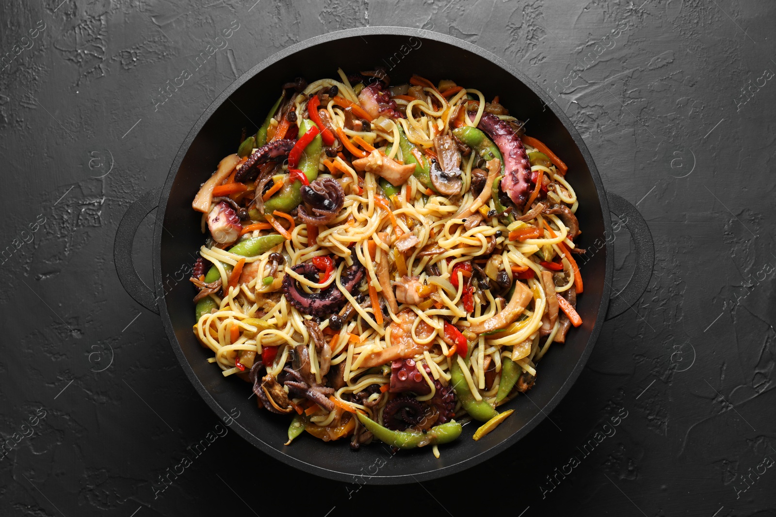 Photo of Stir-fry noodles with sea food and vegetables in wok on dark textured table, top view