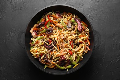 Photo of Stir-fry noodles with sea food and vegetables in wok on dark textured table, top view