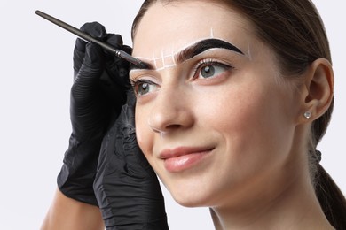 Photo of Young woman undergoing henna eyebrows dyeing procedure on light background, closeup