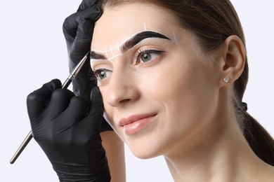 Young woman undergoing henna eyebrows dyeing procedure on light background, closeup