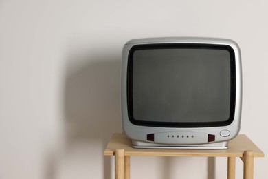 Photo of Retro tv set on wooden shelf against white wall. Space for text