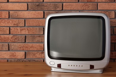 Photo of Retro tv set on wooden shelf against red brick wall. Space for text