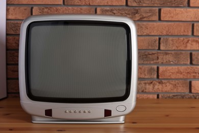 Photo of Retro tv set on wooden shelf against red brick wall. Space for text