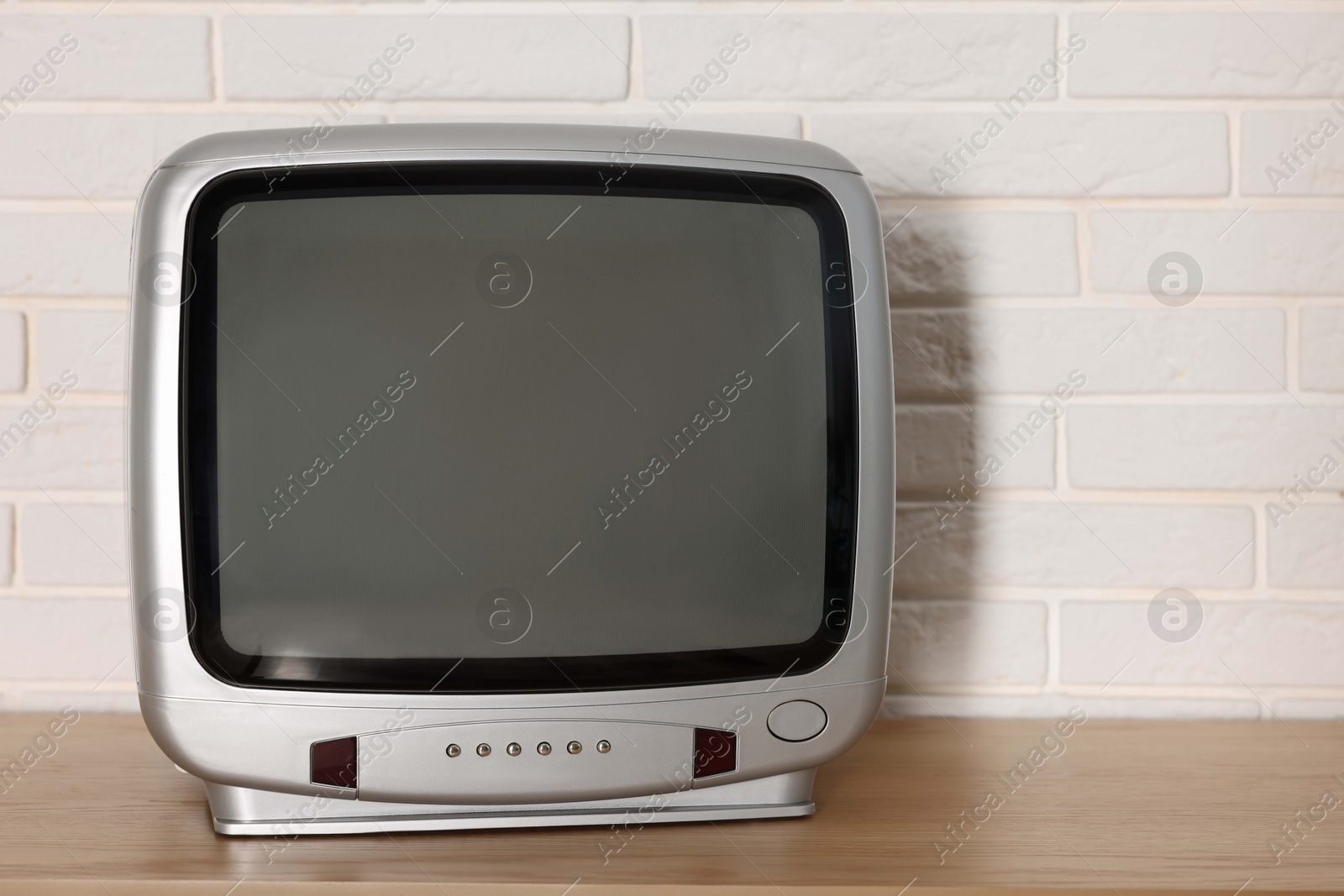 Photo of Retro tv set on wooden shelf against white brick wall. Space for text