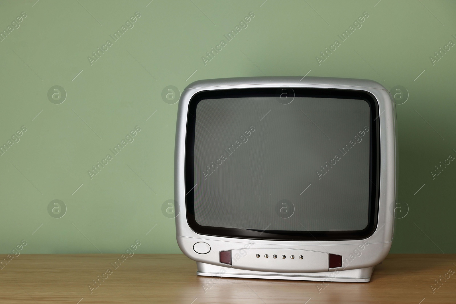 Photo of Retro tv set on wooden shelf against green wall. Space for text