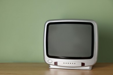 Photo of Retro tv set on wooden shelf against green wall. Space for text