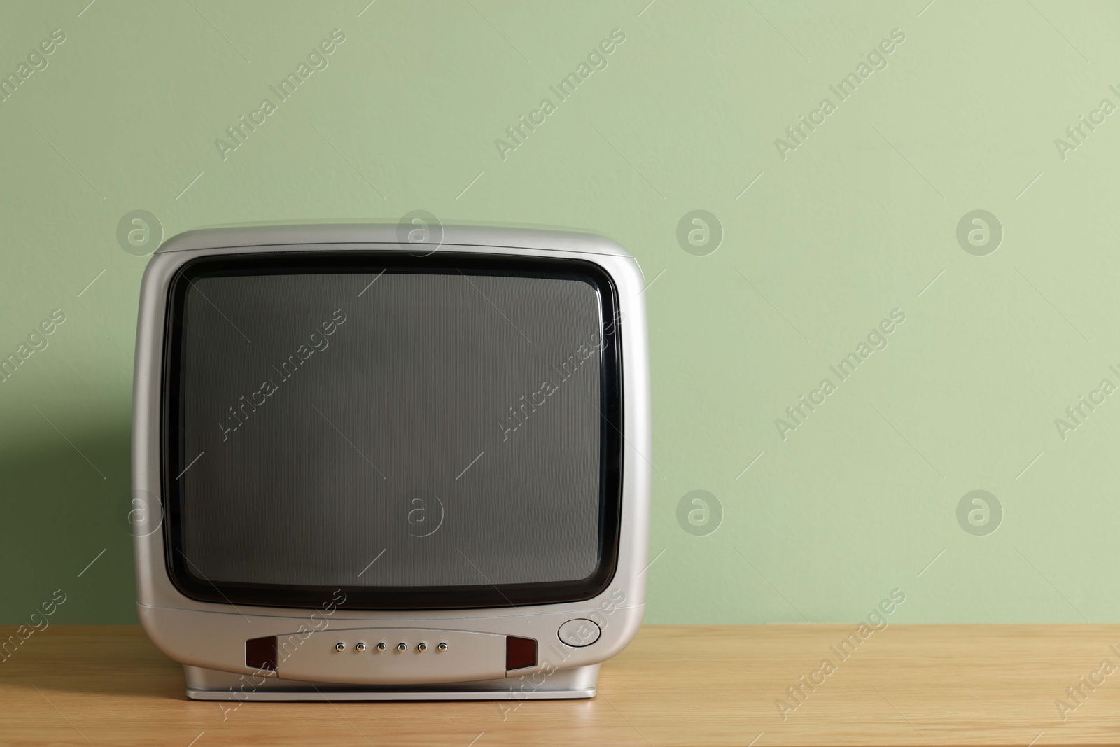 Photo of Retro tv set on wooden shelf against green wall. Space for text