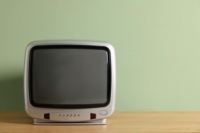 Photo of Retro tv set on wooden shelf against green wall. Space for text