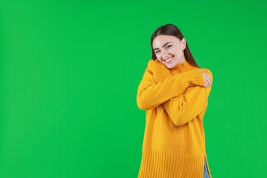 Charming young woman hugging herself on green background. Space for text