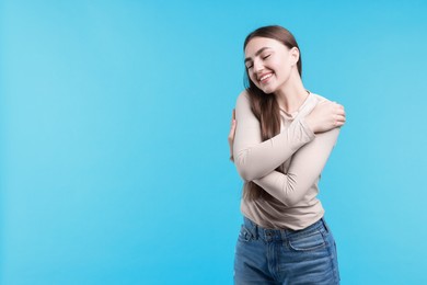 Photo of Charming young woman hugging herself on light blue background. Space for text