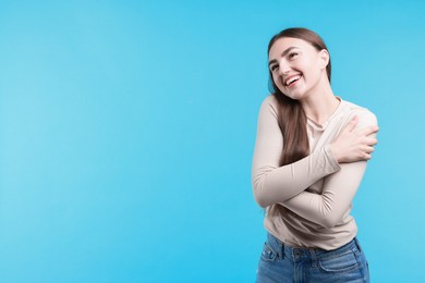 Photo of Charming young woman hugging herself on light blue background. Space for text