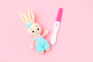 Photo of Pregnancy test and toy bunny on pink background, top view