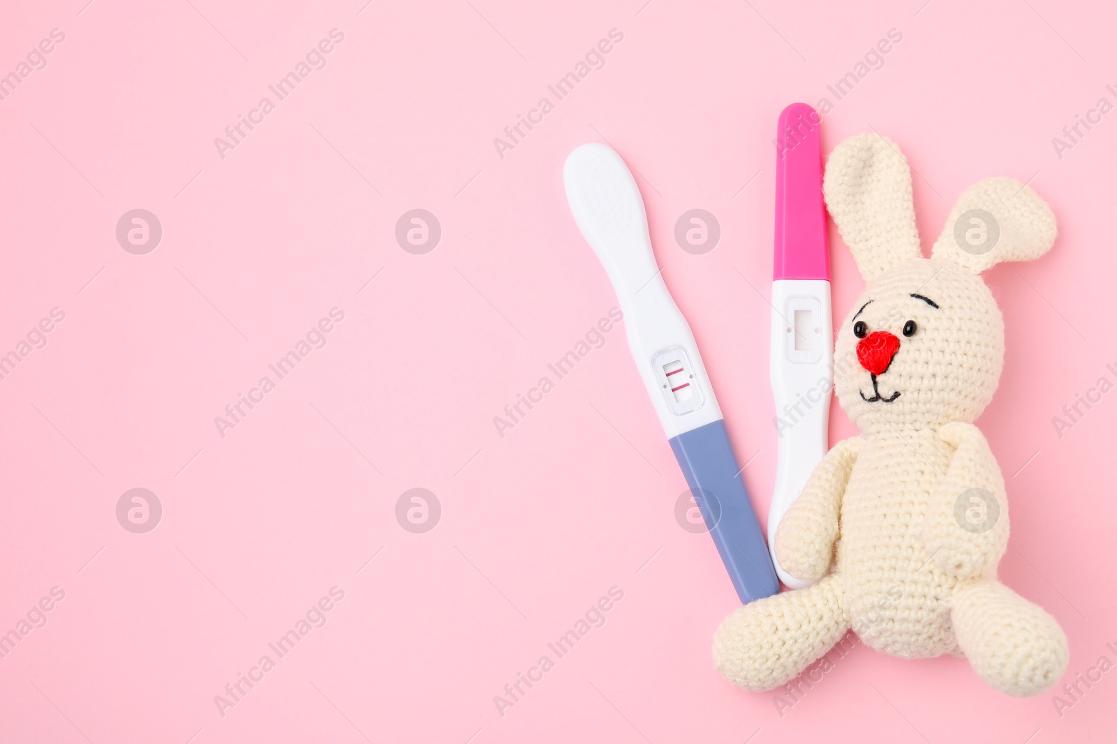 Photo of Pregnancy tests and toy bunny on pink background, top view. Space for text