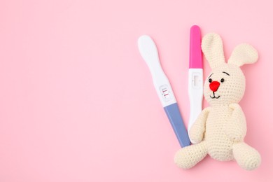 Photo of Pregnancy tests and toy bunny on pink background, top view. Space for text