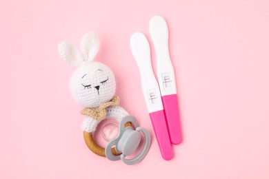 Pregnancy tests, pacifier and baby rattle on pink background, top view