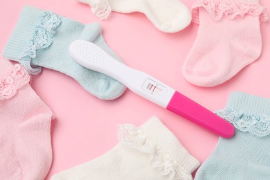 Photo of Pregnancy test and socks on pink background, closeup