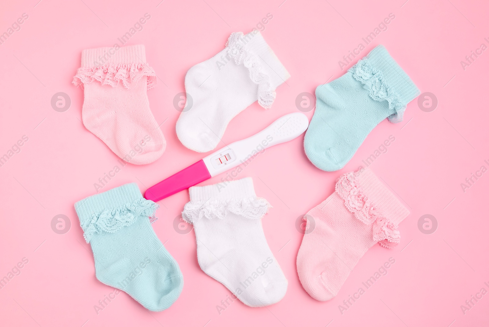 Photo of Pregnancy test and socks on pink background, flat lay