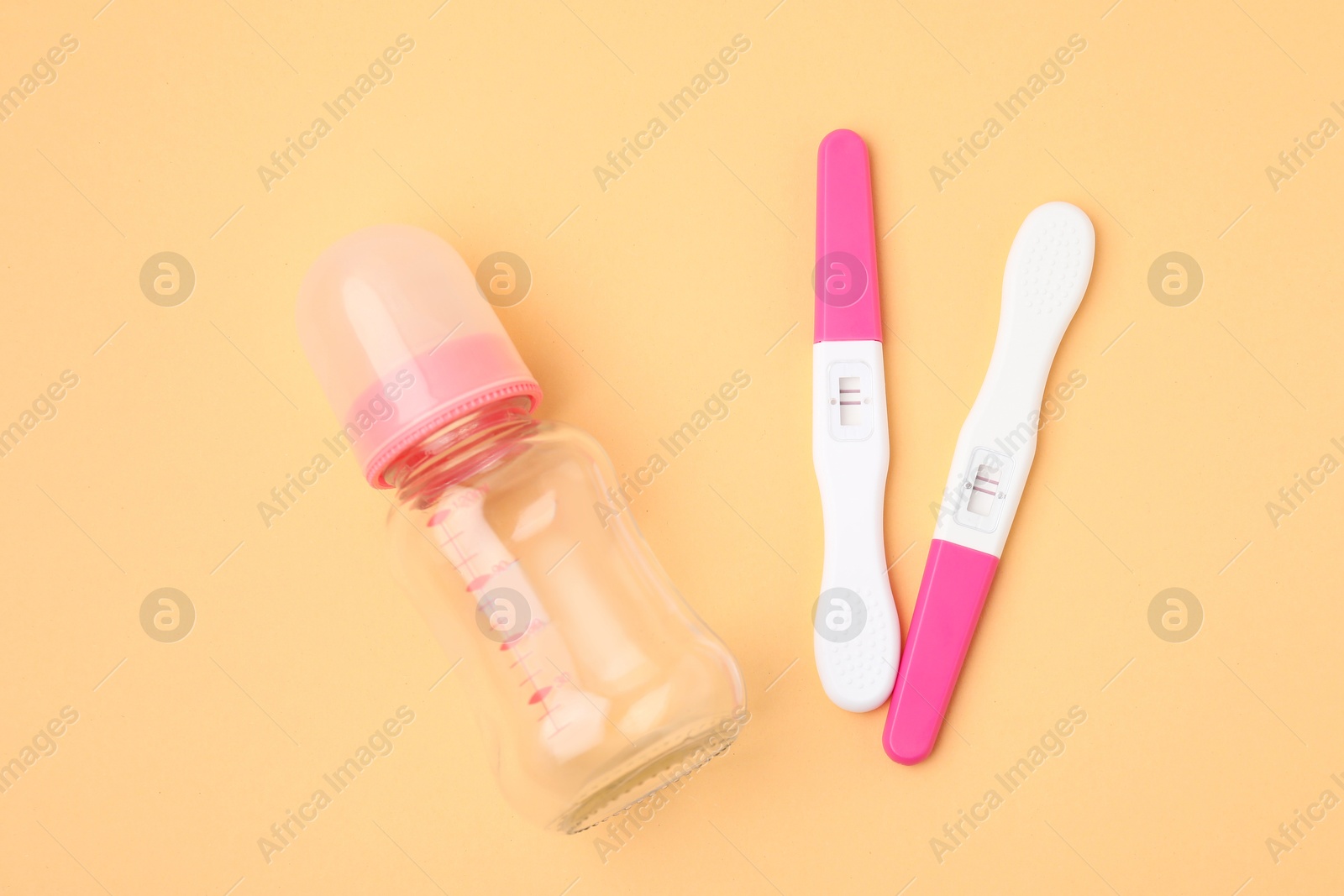 Photo of Pregnancy tests and baby bottle on pale orange background, top view