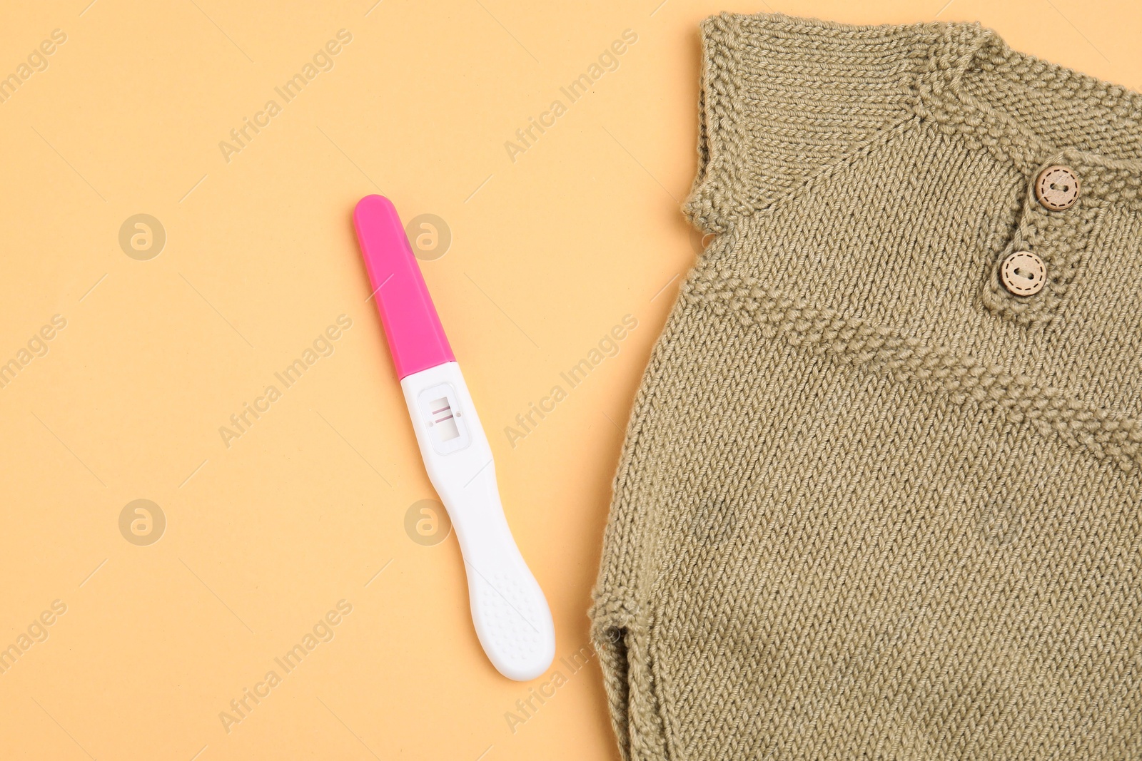 Photo of Pregnancy test and baby clothes on pale orange background, top view