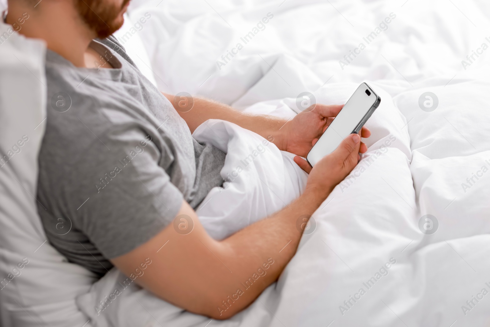 Photo of Man using smartphone in bed, closeup view