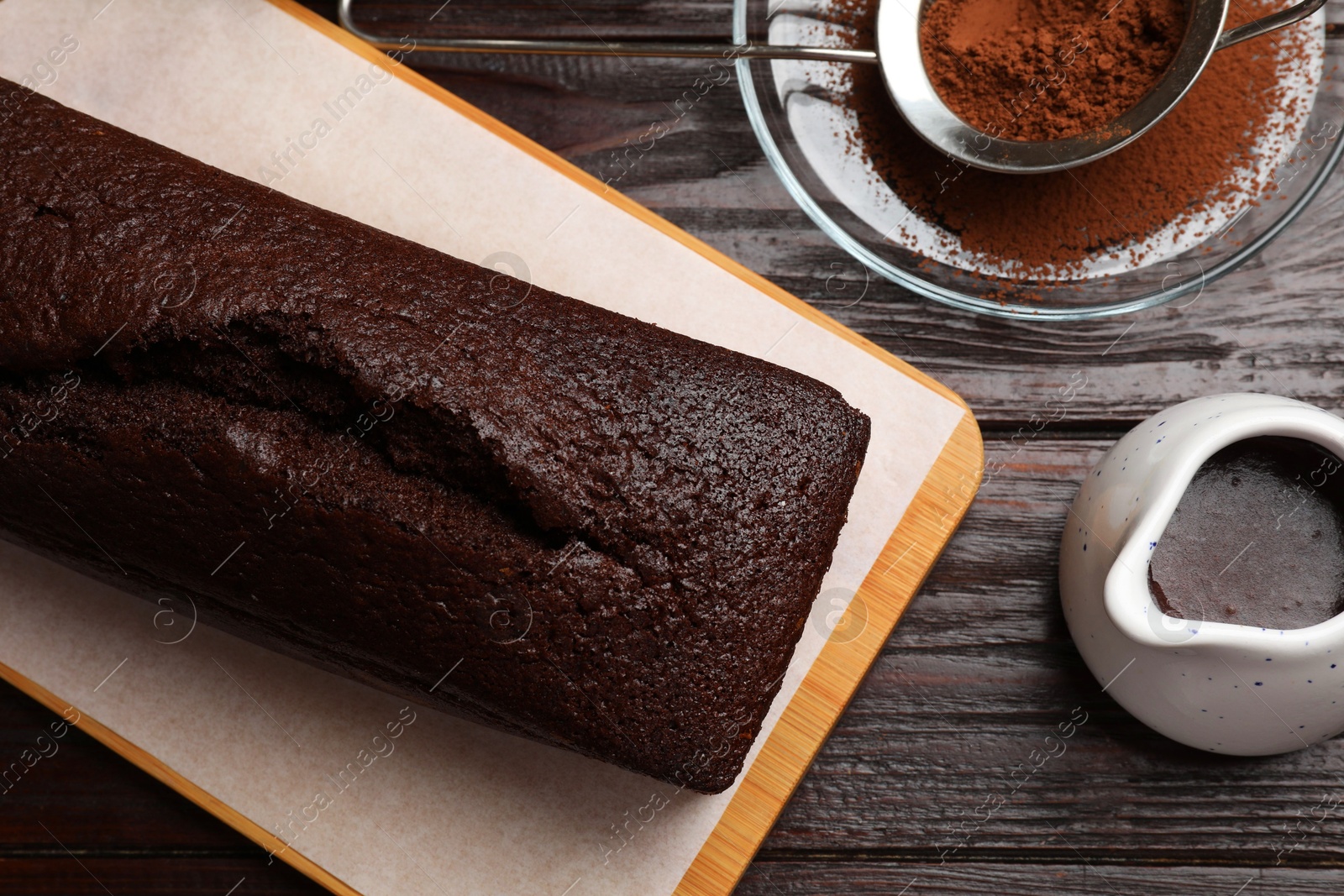 Photo of Tasty chocolate sponge cake and ingredients on wooden table, flat lay