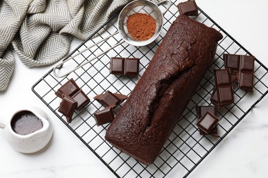 Photo of Tasty chocolate sponge cake and ingredients on white marble table, flat lay