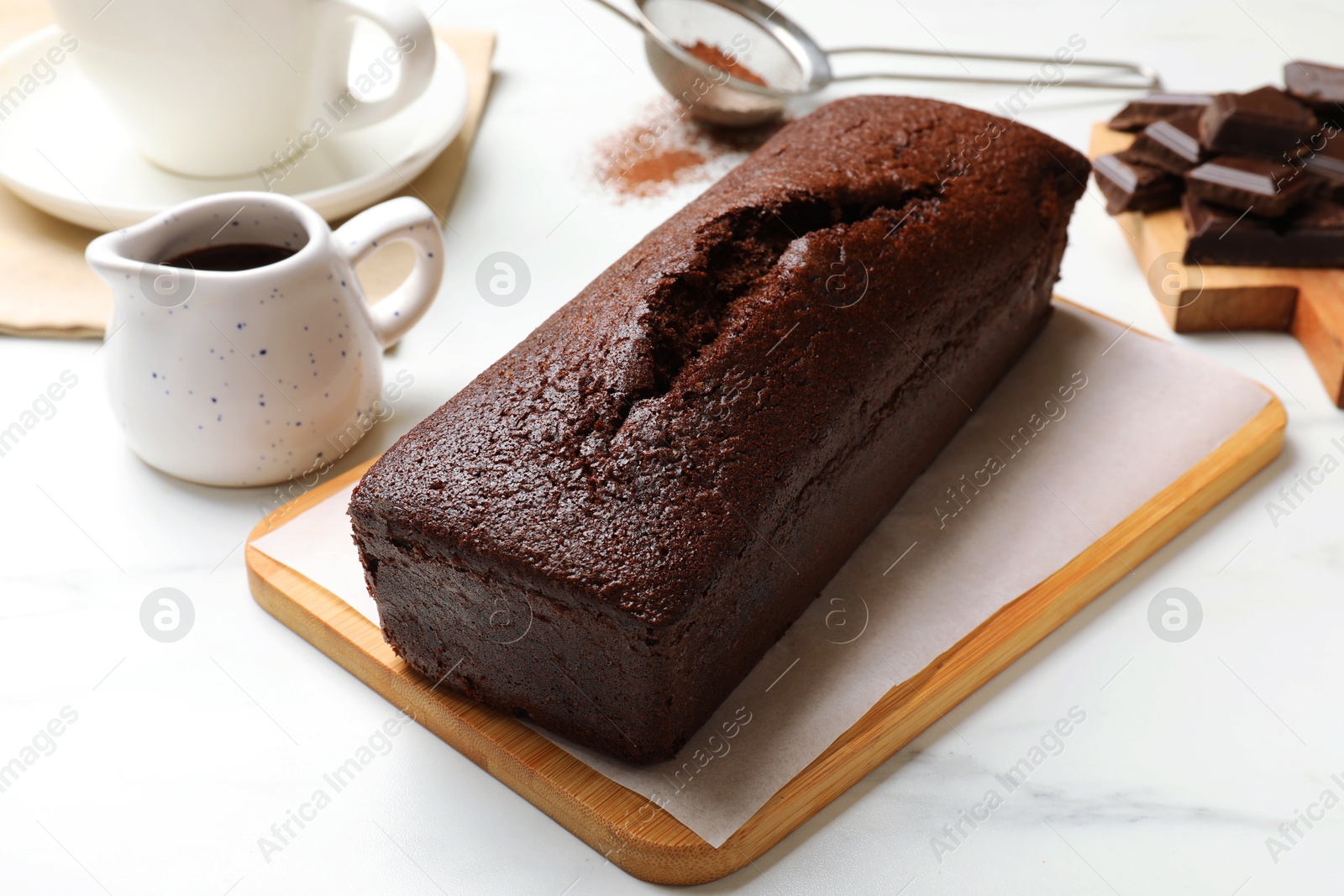 Photo of Tasty chocolate sponge cake and ingredients on white marble table, closeup