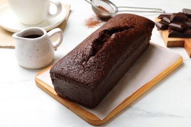 Photo of Tasty chocolate sponge cake and ingredients on white marble table, closeup