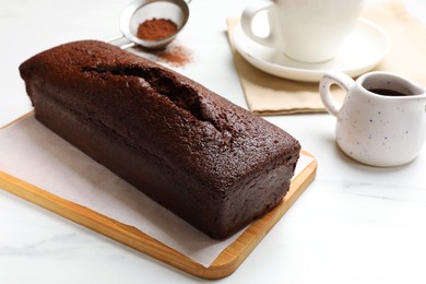 Photo of Tasty chocolate sponge cake and ingredients on white marble table, closeup