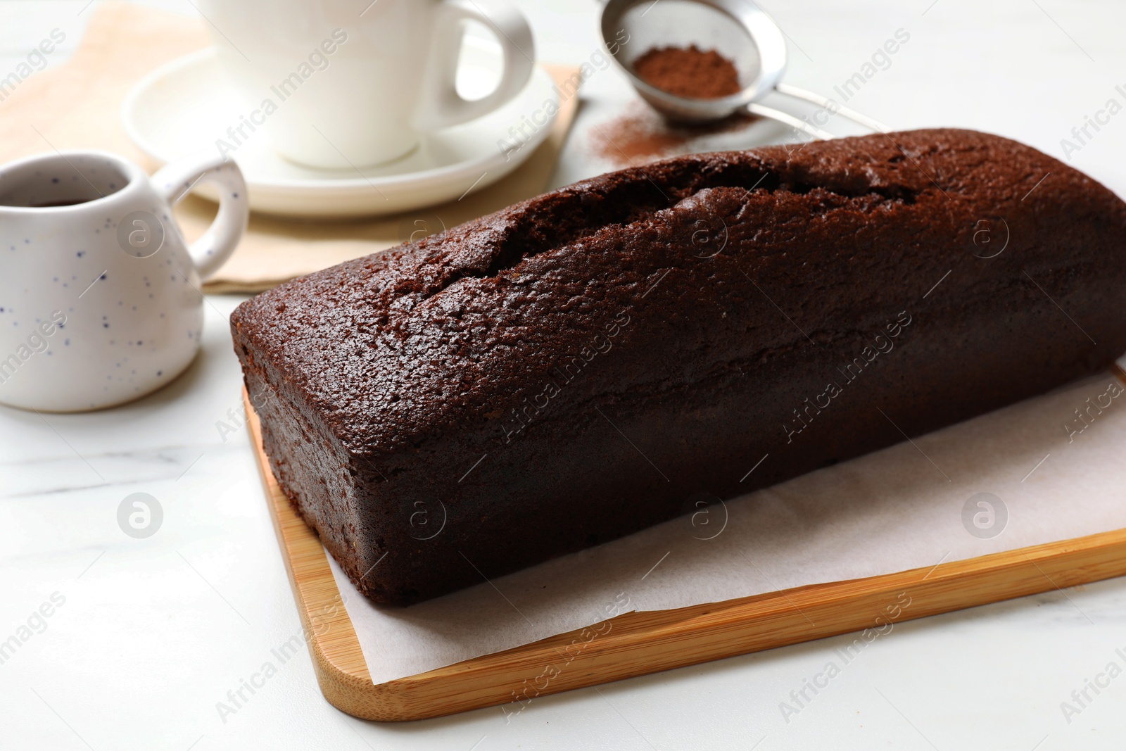 Photo of Tasty chocolate sponge cake and ingredients on white marble table, closeup