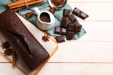 Photo of Tasty chocolate sponge cake and ingredients on white wooden table, flat lay. Space for text